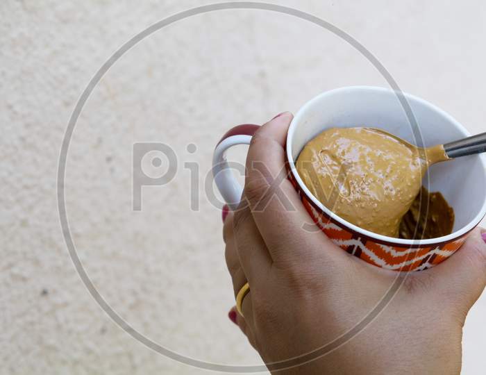 A Girl Showing Thick Hand Beaten Coffee Paste In A Colorful Mug Against Plain Wall Background