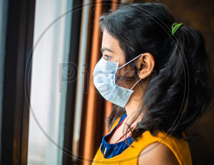 Coronavirus. Sick Young Girl Of Corona Virus Looking Through The Window And Wearing Mask Protection And Recovery From The Illness In Home. Quarantine. Patient Isolated In House To Prevent Infection.