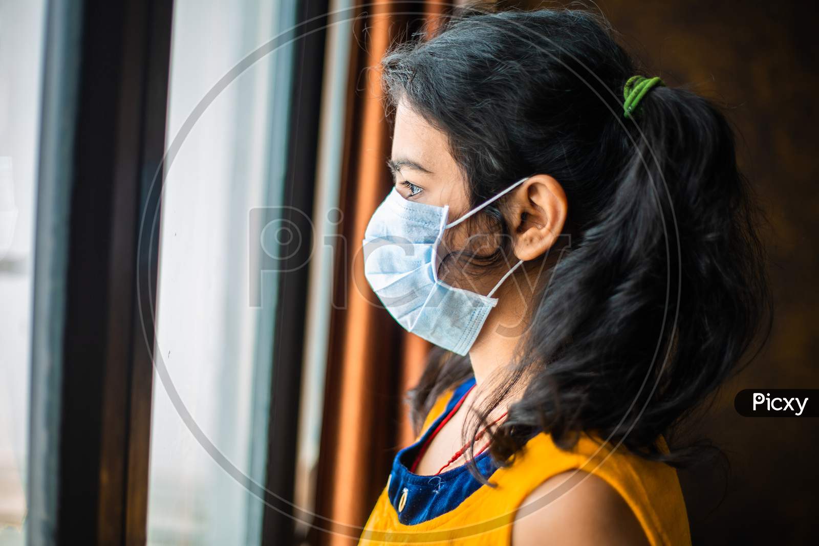 Coronavirus. Sick Young Girl Of Corona Virus Looking Through The Window And Wearing Mask Protection And Recovery From The Illness In Home. Quarantine. Patient Isolated In House To Prevent Infection.