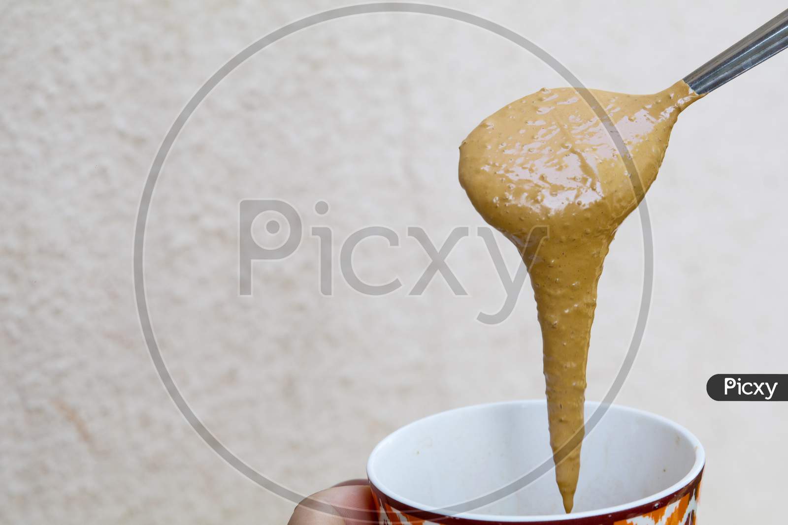 A Girl Showing Thick And Creamy Hand Beaten Coffee Paste In A Colorful Mug Against Plain Wall Background
