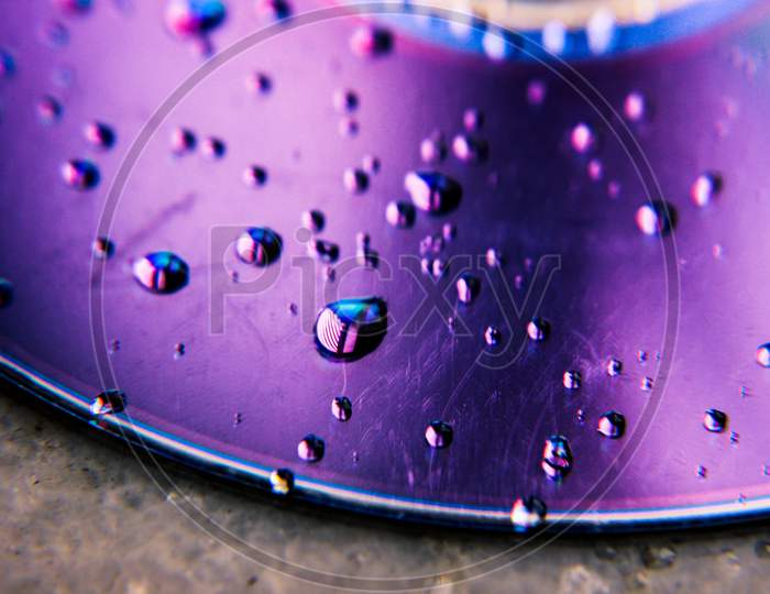 Water drops on disk, Selective focus on water drops with blurred disk background ,Vibrant color reflection on water drops, scratches on disk CD/DVD