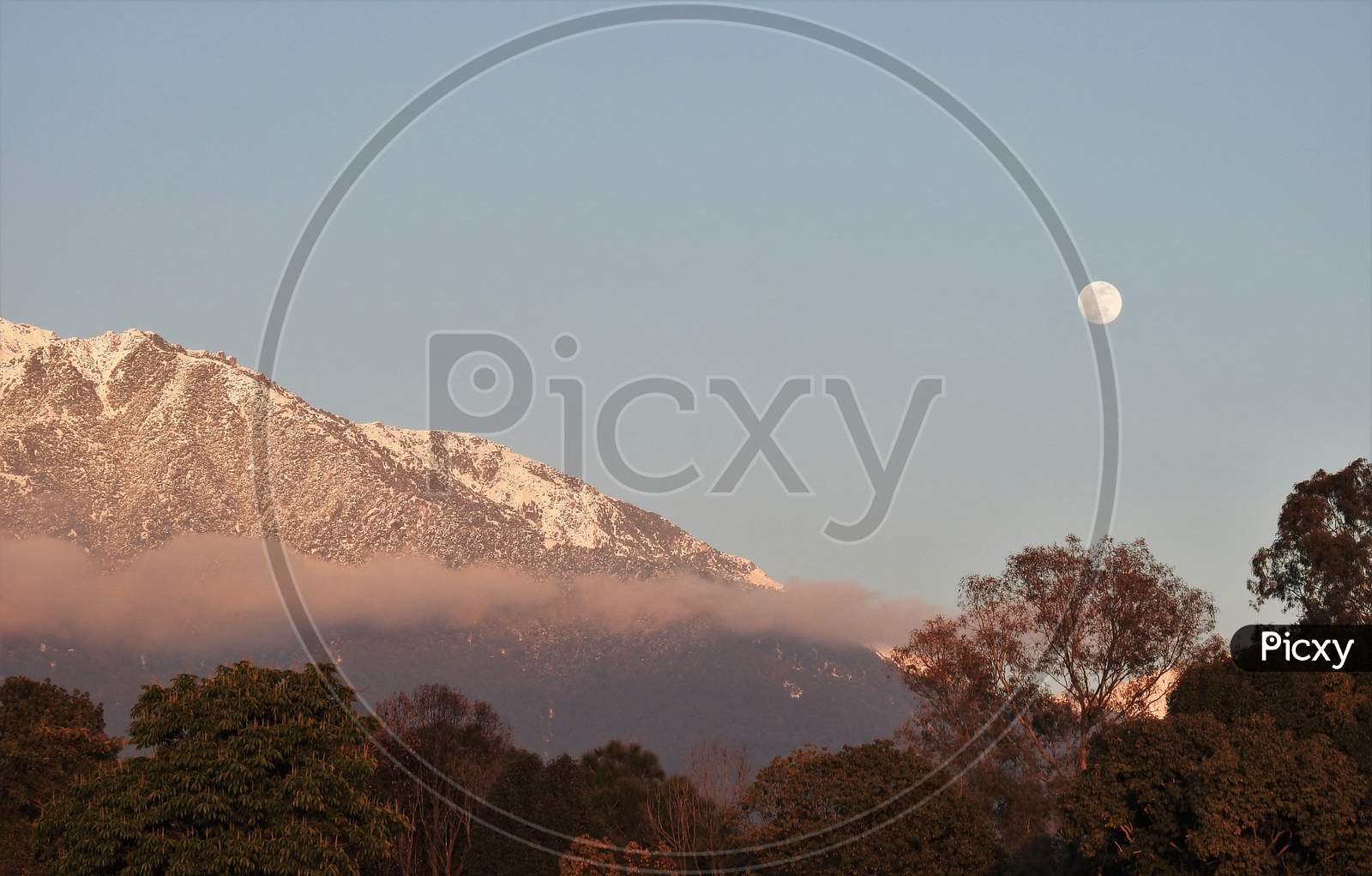 Moon in sky with snow capped hill