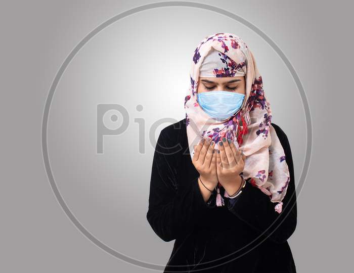 Muslim Woman Wearing Medical Mask for Protection from Infection From Coronavirus(Covid-19) Prays to Allah. Isolated Grey Background.