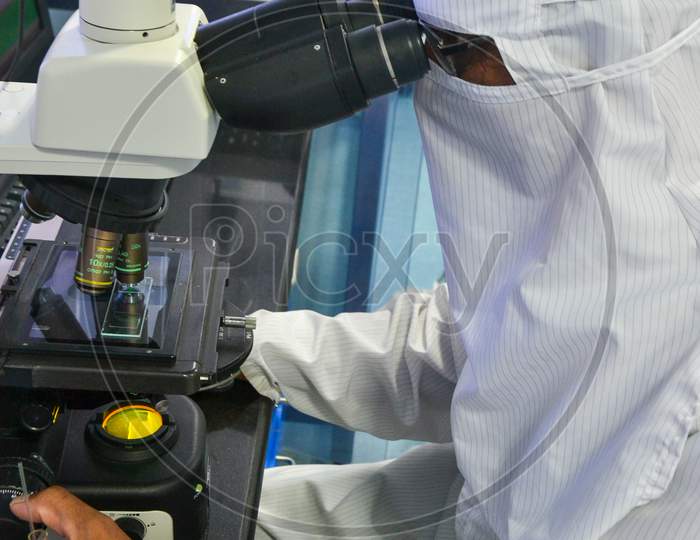 Scientist in protective coverall doing research and testing through microscope at a laboratory in India, while maintaining quality standards and protocols, PPE, personal protective equipment