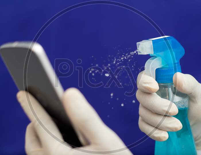 Doctor Cleaning Mobile Phone To Eliminate Covid-19 - Nurse Hands With Gloves Cleaning The Phone By Liquid Sanitizer At Hospital - Alcohol To Wipe Contamination With Coronavirus