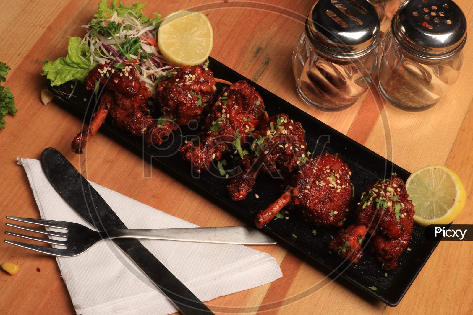 Chicken lollipop is Indian Chinese appetizer which is a frenched chicken winglet. wrapped with silver foil at one end & surved with chutney. Over colourful or wooden background. Selective focus.