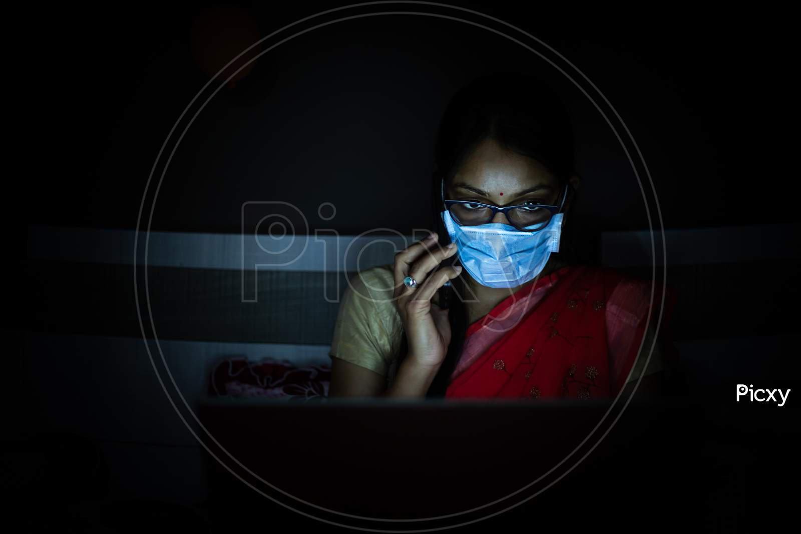 Young Indian Woman Wearing Mask Working On Her Laptop And Talking On Phone, Late Night Working, Freelancer Working From Home. Coronavirus,Covid-19. Stay Home Stay Safe, Woman In Quarantine.