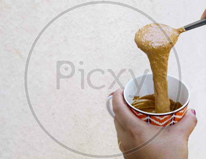 A Girl Showing Hand Beaten Coffee Paste In A Colorful Mug Against Plain Wall Background
