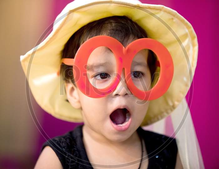 Indian Kid Wearing Big Glasses And Cap Giving Wow Expression With open mouth During Party