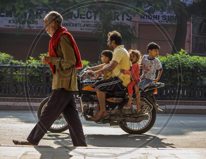 september 2018, hawa mahal road, jaipur rajasthan india : old man walks on a street and a man riding a bike with his family  