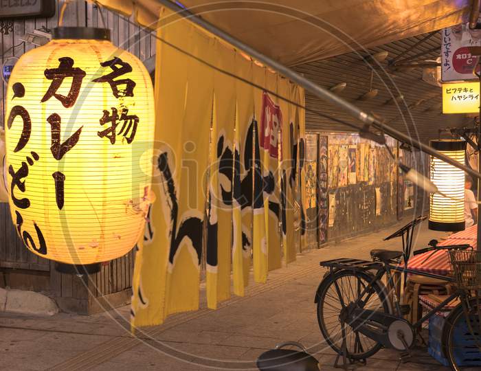 Night view of a traditional retro yellow rice paper lantern where it is written "Meibutsu Kare Udon" which means "Curry noddles Specialty" on underpass Yurakucho Concourse under the railway line of the station Yurakucho.