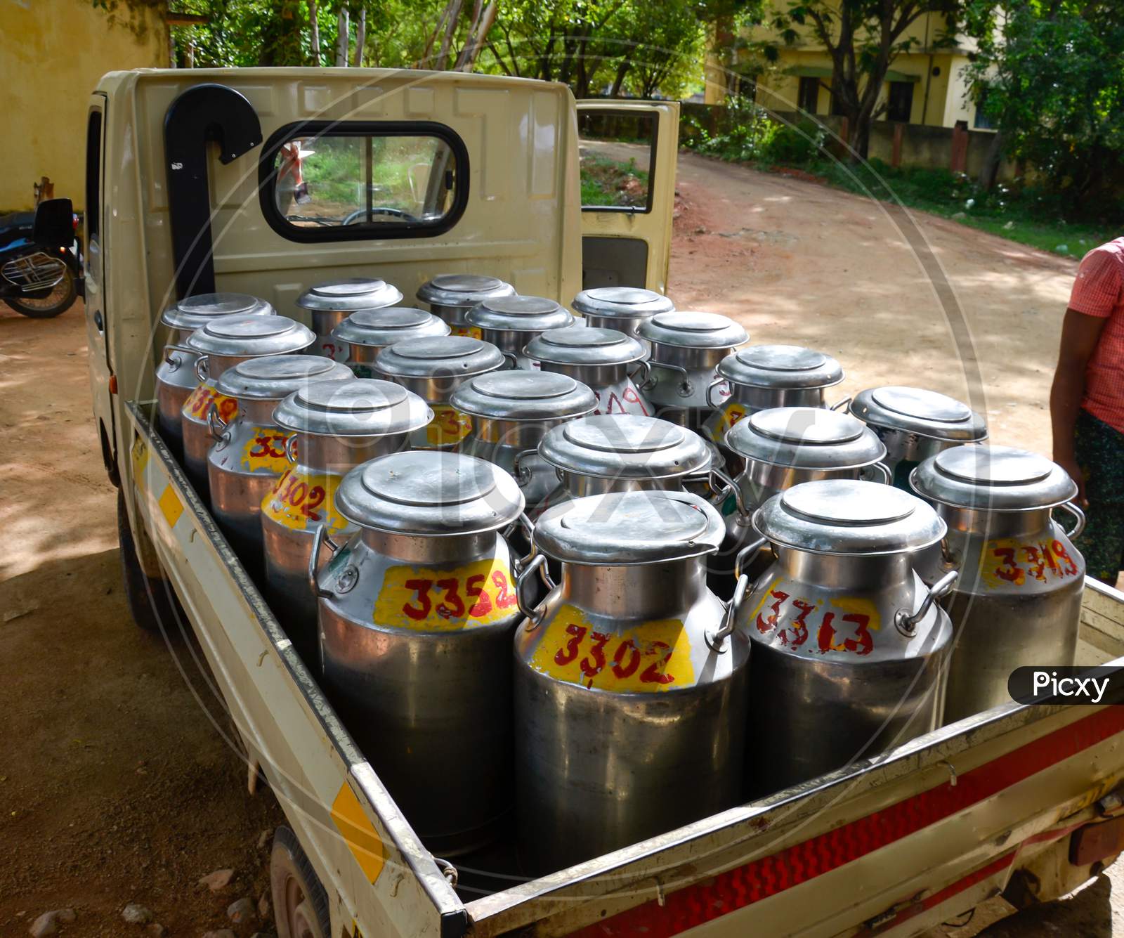 Individually numbered stainless steel milk cans filled with raw milk loaded in a mini truck in India