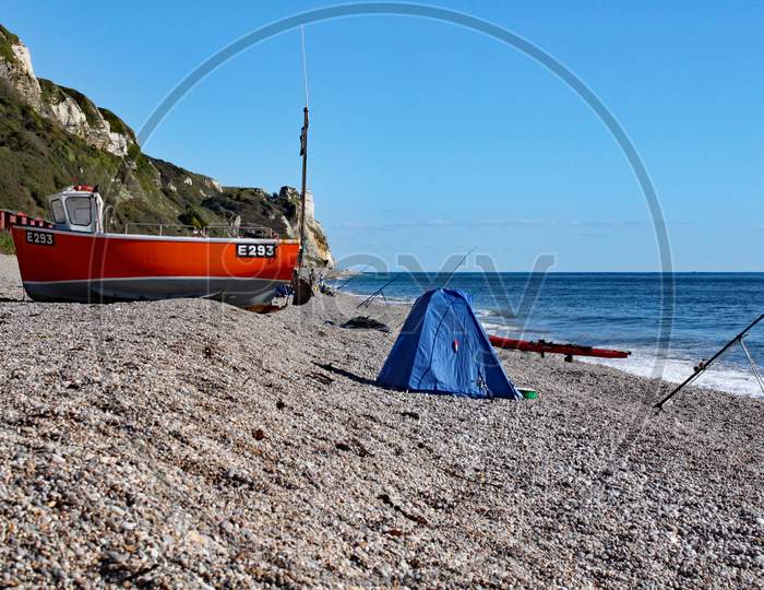 An Old Boat On The Beach At Branscombe In Devon, England. Fishermen'S Equipment Stands In The Foreground.