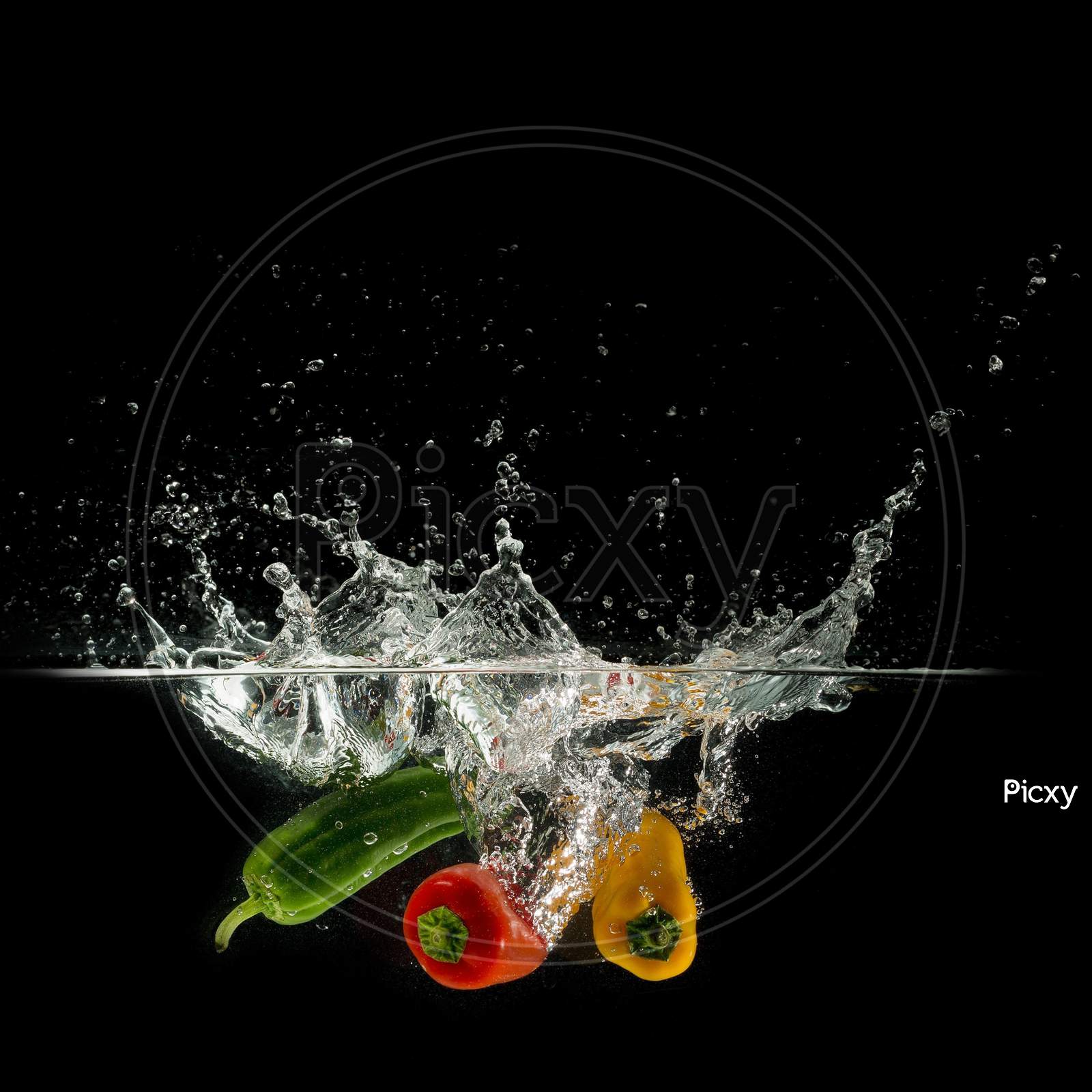 Three Paprika Splash In Water On Black Background, Capsicum Annuum: Bell Pepper And Buble.