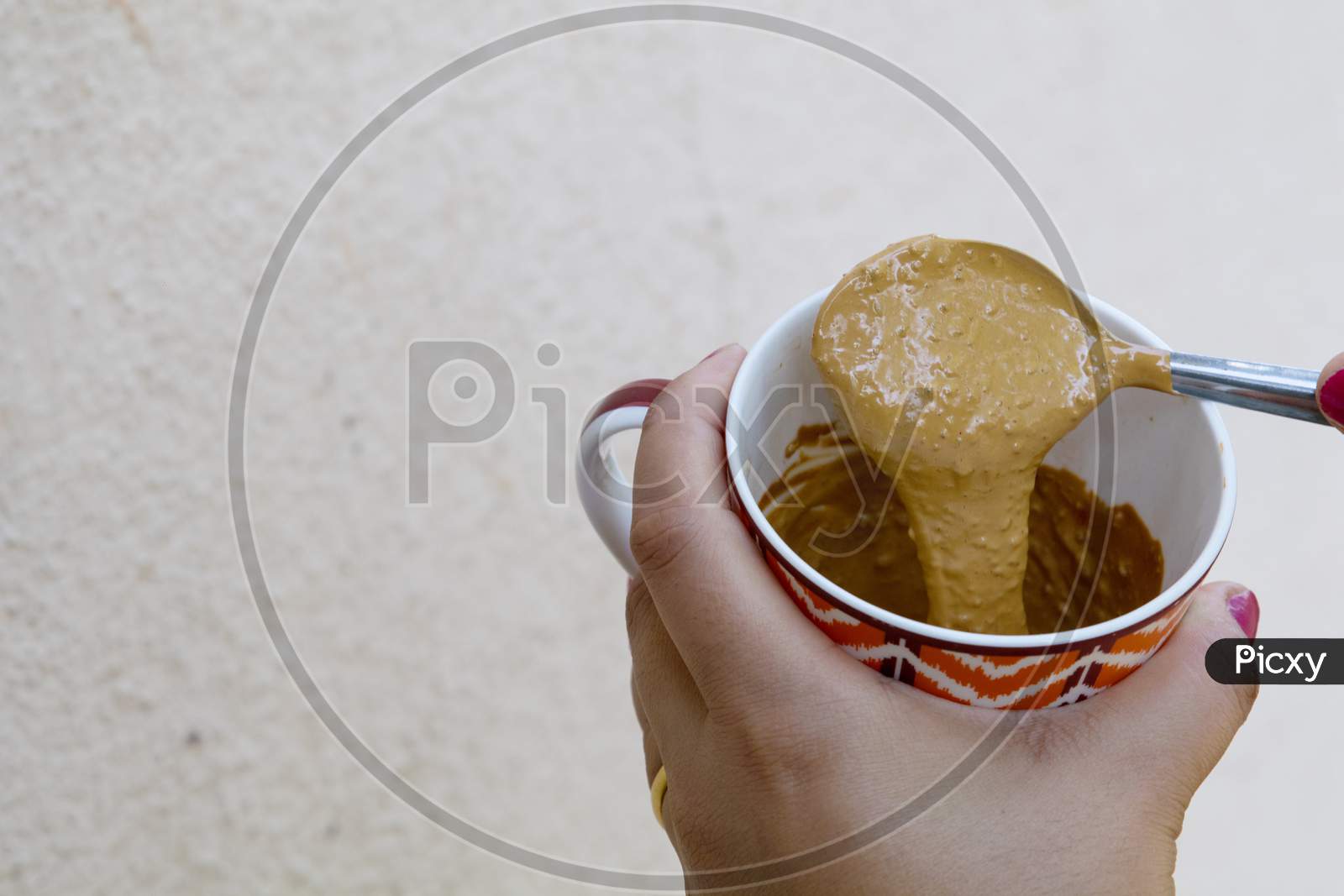 A Girl Showing Thick Hand Beaten Coffee Paste In A Colorful Mug Against Plain Wall Background