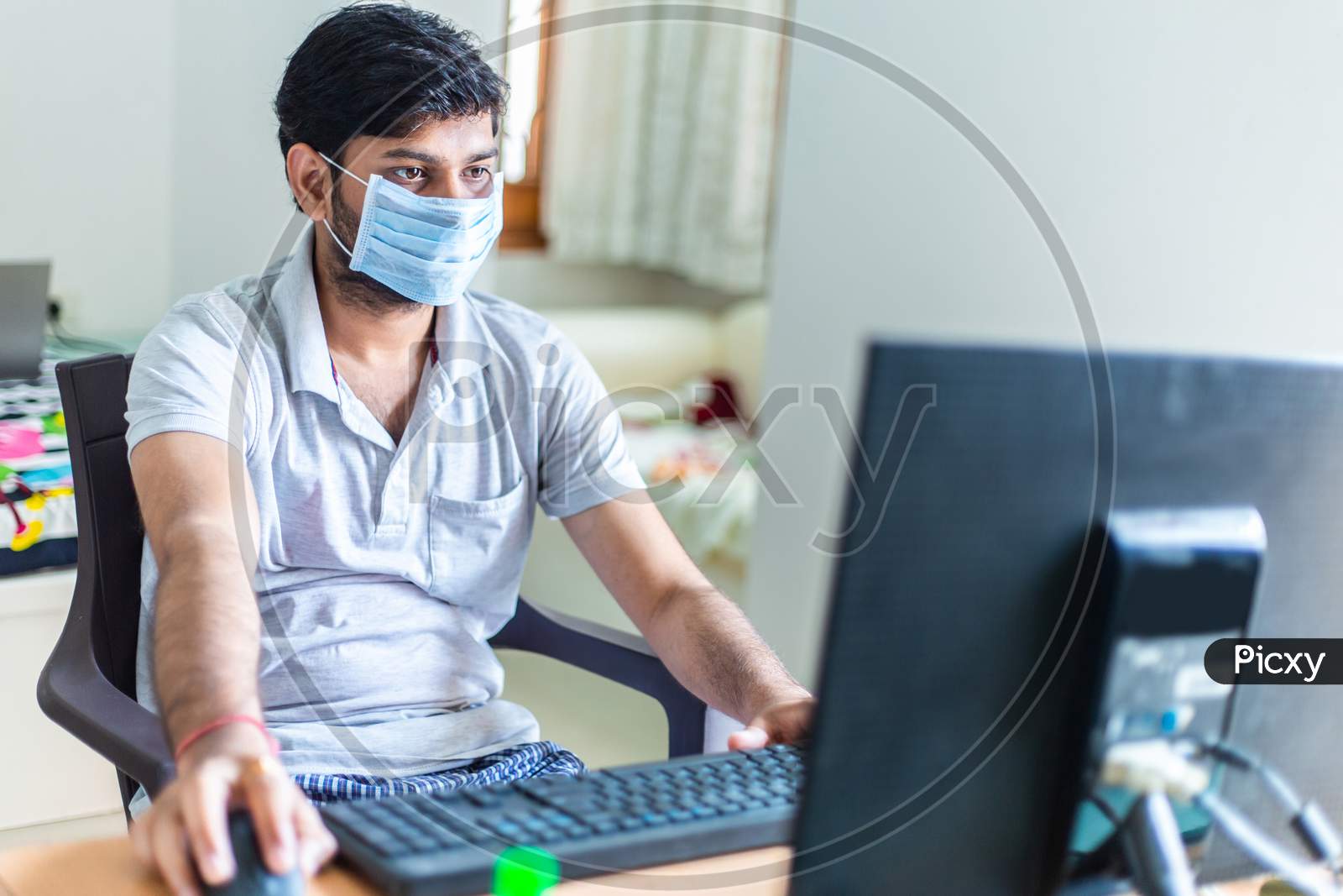 Young Man Quarantined At Home During World Pandemic Of Coronavirus Covid-19 Prevention. Stay At Home, Stay Safe. Man With Protective Medical Mask Using Computer. Isolation, Lock Down Situation.
