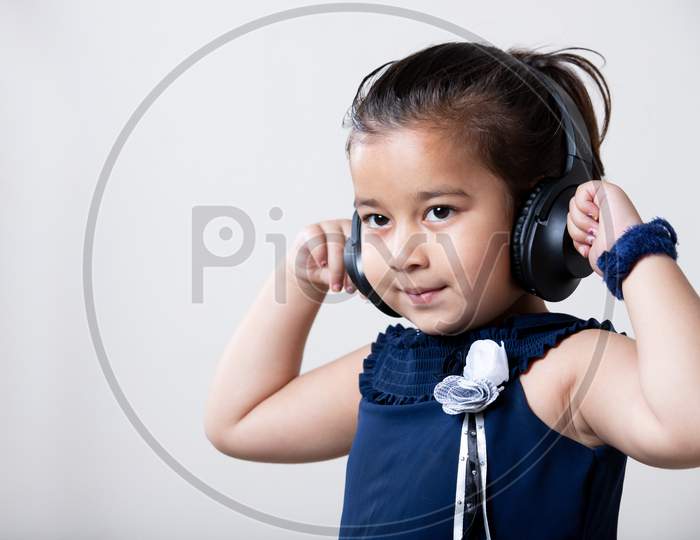 Asian Little Girl Listing Music On Wire Less Headphone With Hands On Ear.