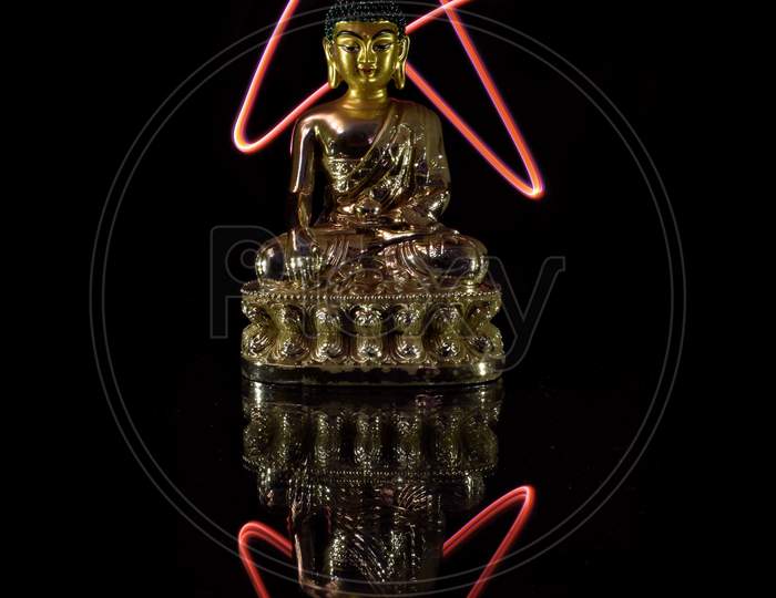 Buddha statue is placed on a glass with star painted black background and reflection.