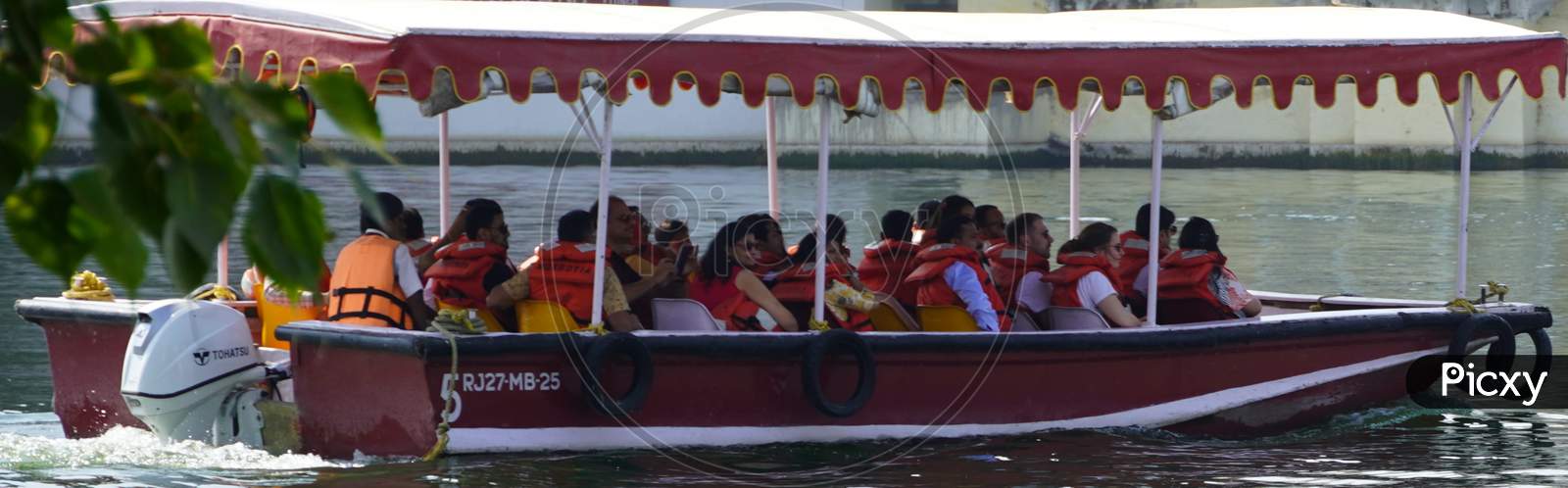 Side View Of Passenger Transportation With Boat, Water Taxi Trip. People Wearing Life Jackets Traveling In Public Ferry Boat. Group Of Passengers Sitting On Benches : Udaipur India - February 2020
