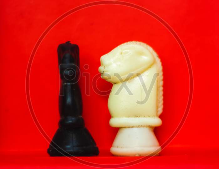Chess Pieces Knights Facing Each Other For A Standoff With Blurred Isolated On Red Background. Confrontation Of Chess Pieces.Chess Pieces Knights On Chess War Field. Chess Knights Head To Head