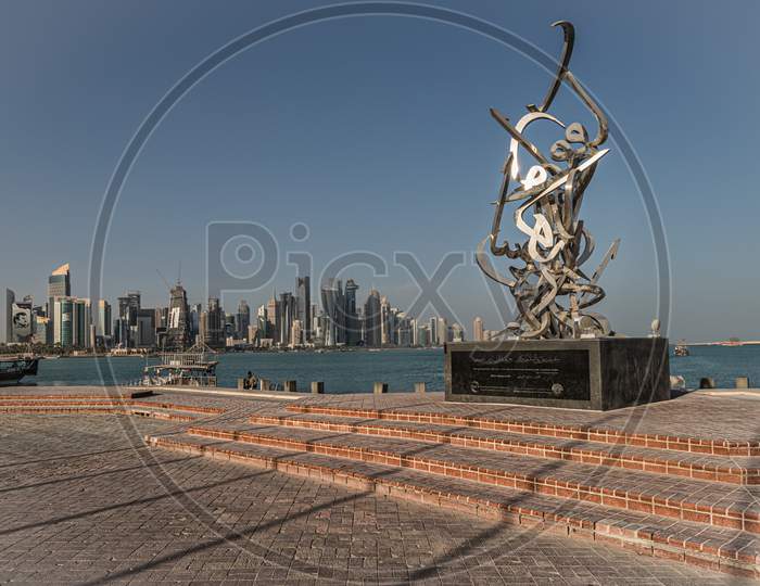 Doha Qatar skyline daylight view showing skyscrapers and dhows in background and Calligraphy sculpture in foreground