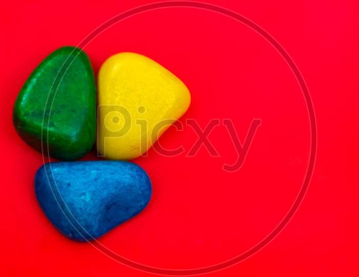 Multi Color Natural Pebbles Green, Blue And Yellow Stone Isolated On Red Background With Space For Copy Text And Words. Colorful Natural Pebbles Stone Isolated. Colorful Sea Stones. Rgb Color Stones.