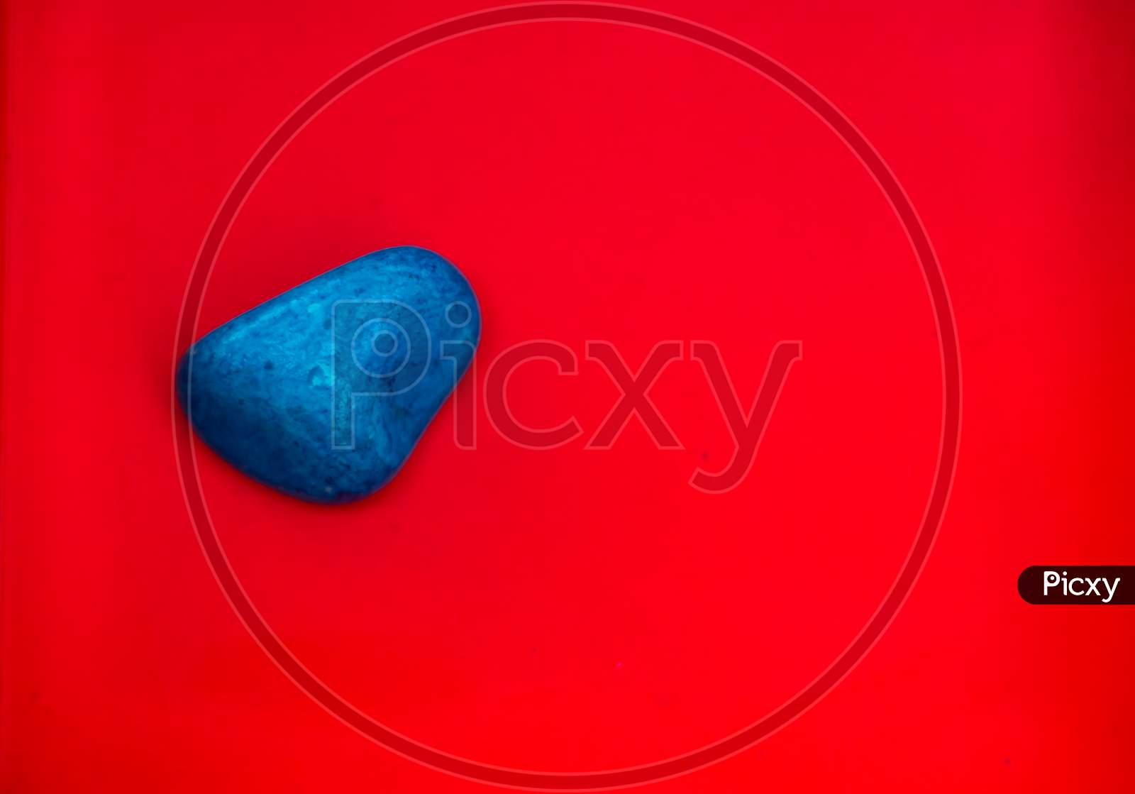 Blue Color Natural Pebbles Isolated On Red Background With Space For Copy Text And Words. Multi Color Natural Pebbles Stone. Blue Color Stone Isolated. Colorful Sea Stones