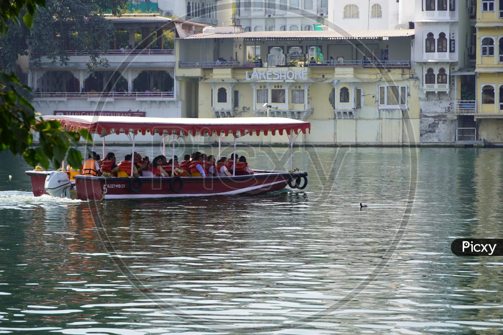 Side View Of Passenger Transportation With Boat, Water Taxi Trip. People Wearing Life Jackets Traveling In Public Ferry Boat. Group Of Passengers Sitting On Benches : Udaipur India - February 2020