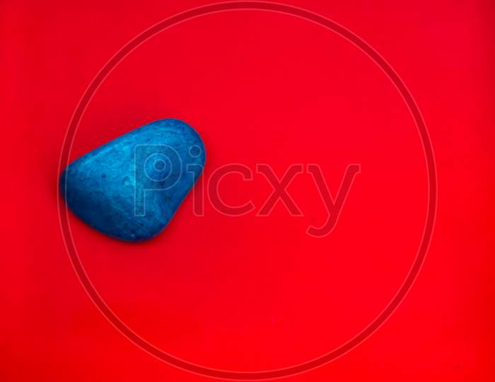 Blue Color Natural Pebbles Isolated On Red Background With Space For Copy Text And Words. Multi Color Natural Pebbles Stone. Blue Color Stone Isolated. Colorful Sea Stones