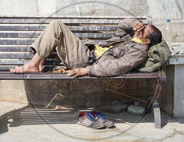 Poor Homeless Beggar Man Or Refugee Sleeping On A Dirty Wooden Bench In A One-Way Street In The City During Day Time. Social Documentary Concept. Shoes On Floor. - Udaipur India : February 2020