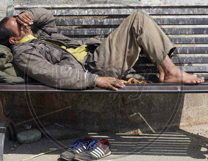 Poor Homeless Beggar Man Or Refugee Sleeping On A Dirty Wooden Bench In A One-Way Street In The City During Day Time. Social Documentary Concept. Shoes On Floor. - Udaipur India : February 2020
