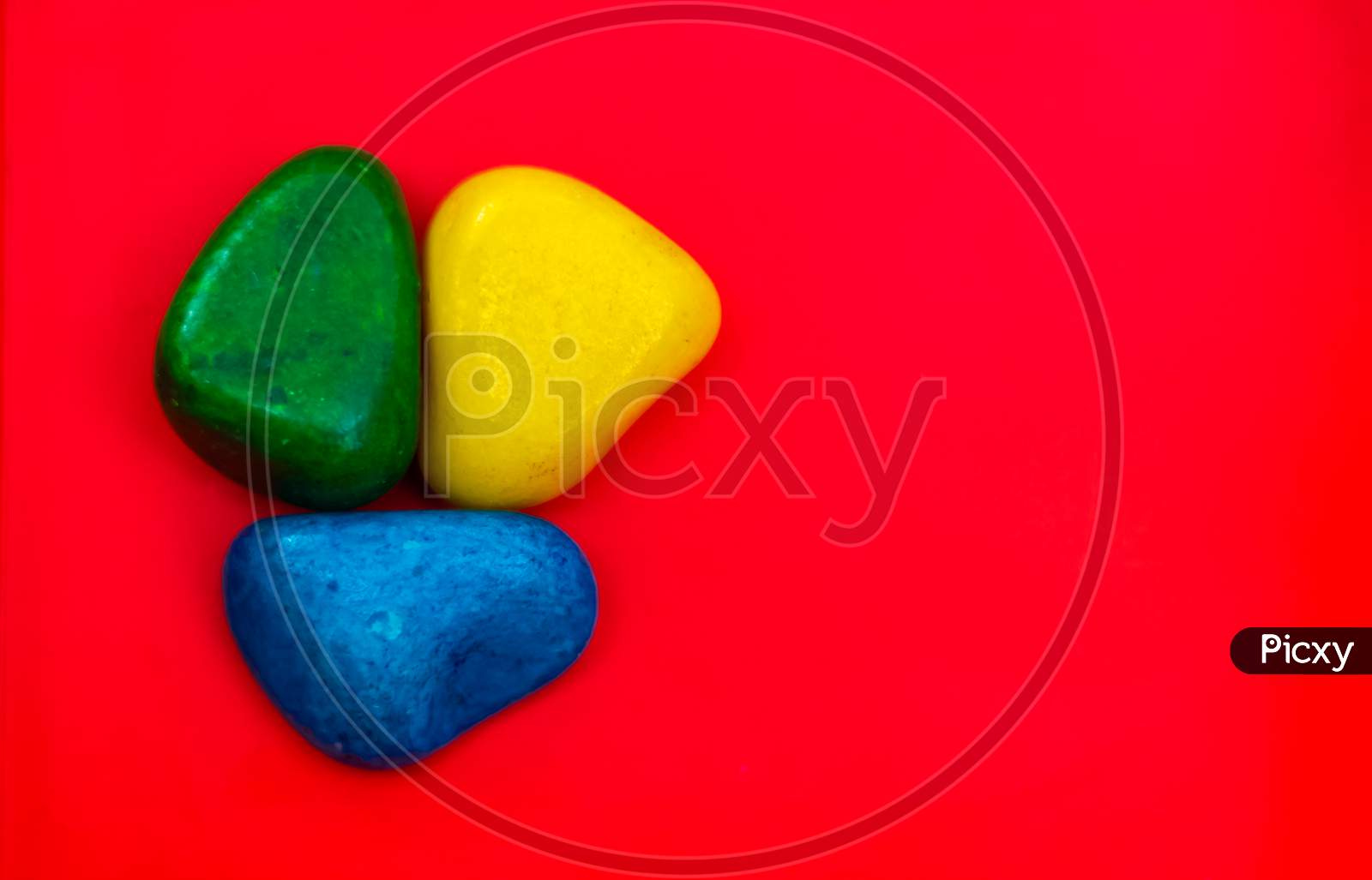Multi Color Natural Pebbles Green, Blue And Yellow Stone Isolated On Red Background With Space For Copy Text And Words. Colorful Natural Pebbles Stone Isolated. Colorful Sea Stones. Rgb Color Stones.