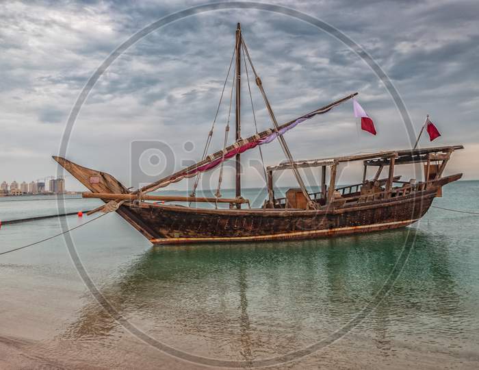 Traditional wooden boat dhow in Katara beach Qatar with Qatar flag and clouds in the sky in background