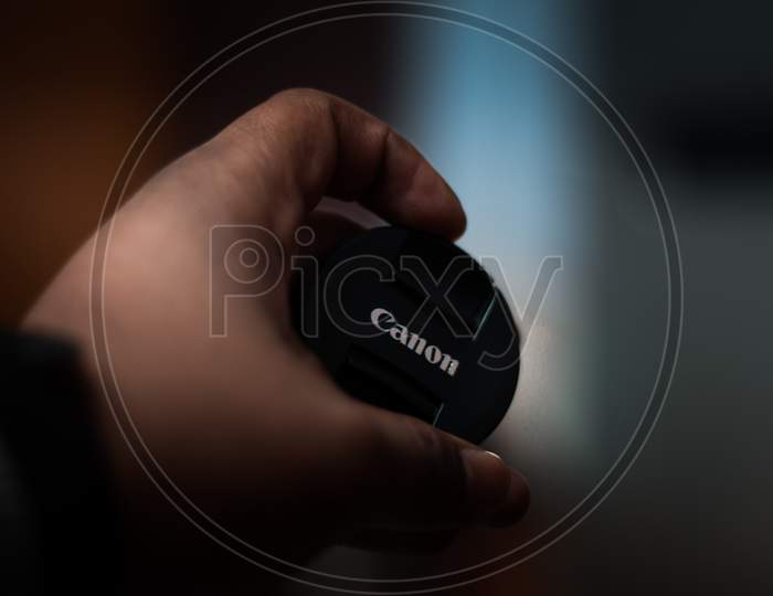 New Delhi, India - March 23 2019 : Holding Canon Lens Cap With Circular Bokeh In The Backgound