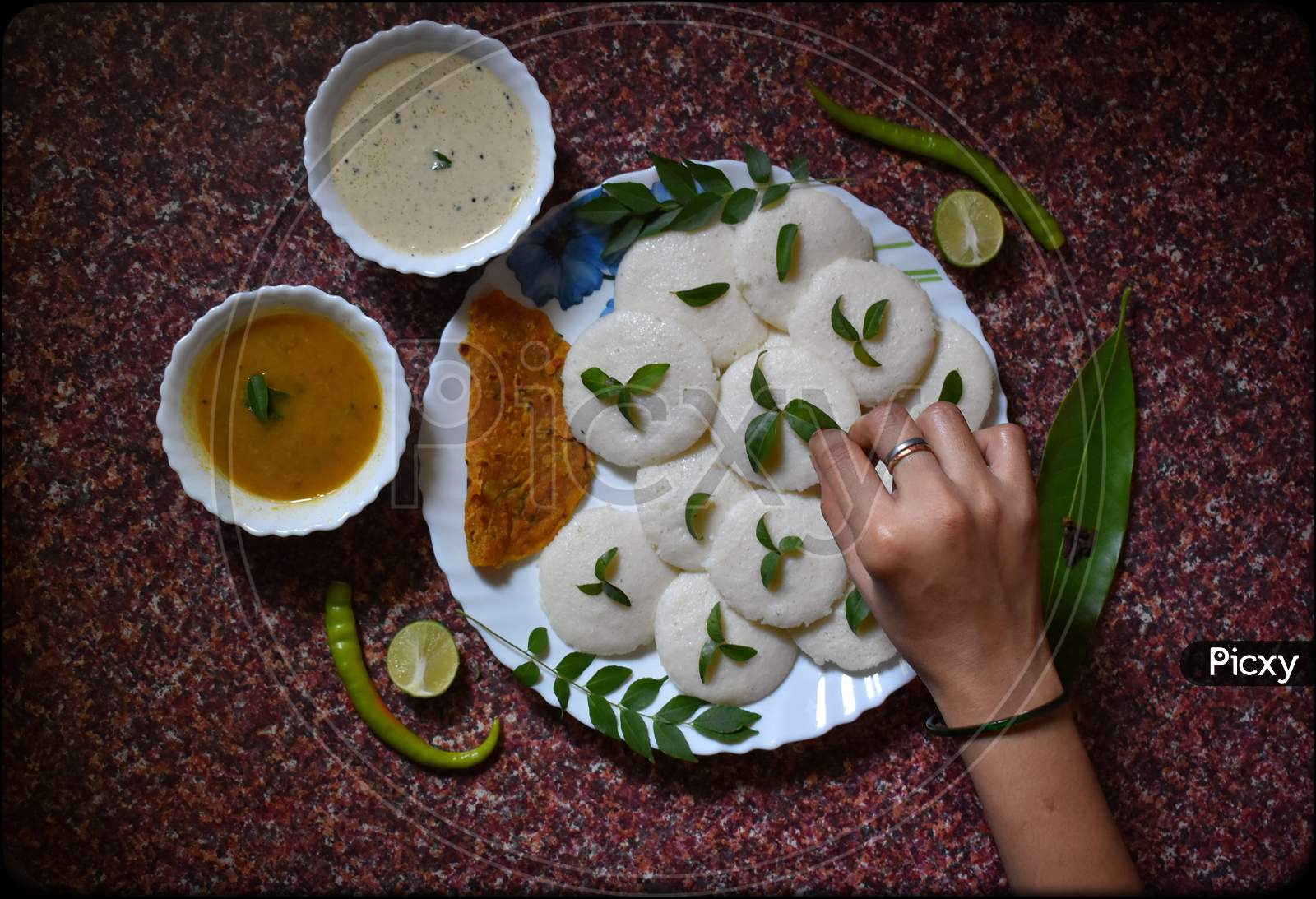 Garnishing idli, chutney and sambhar dish with the stuff of curry leaves