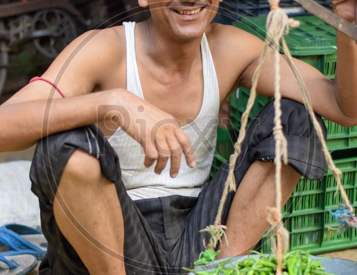 Bareilly, UP, 2018: Asian street vendor holding weighing scale and selling green chilly in the street markets of India