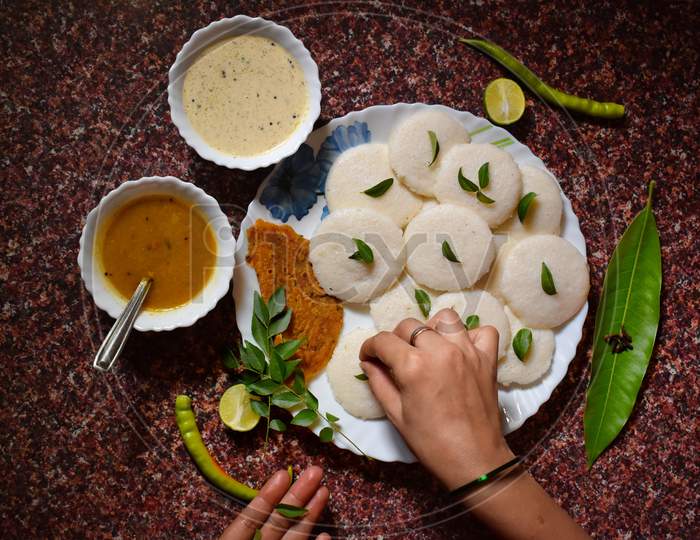 Garnishing idli, chutney and sambhar dish with the stuff of  green chillies and curry leaves