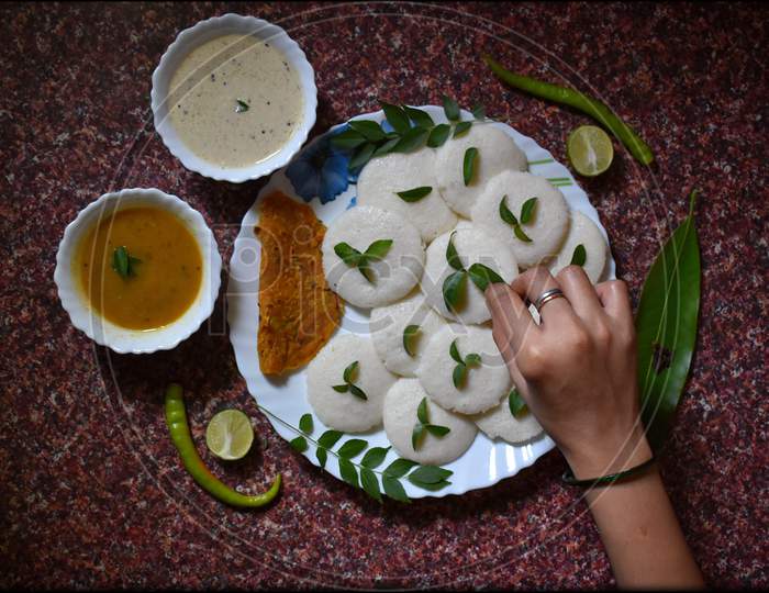 Garnishing idli, chutney and sambhar dish with the stuff of curry leaves