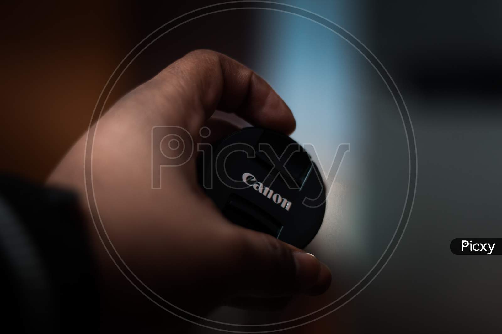 New Delhi, India - March 23 2019 : Holding Canon Lens Cap With Circular Bokeh In The Backgound