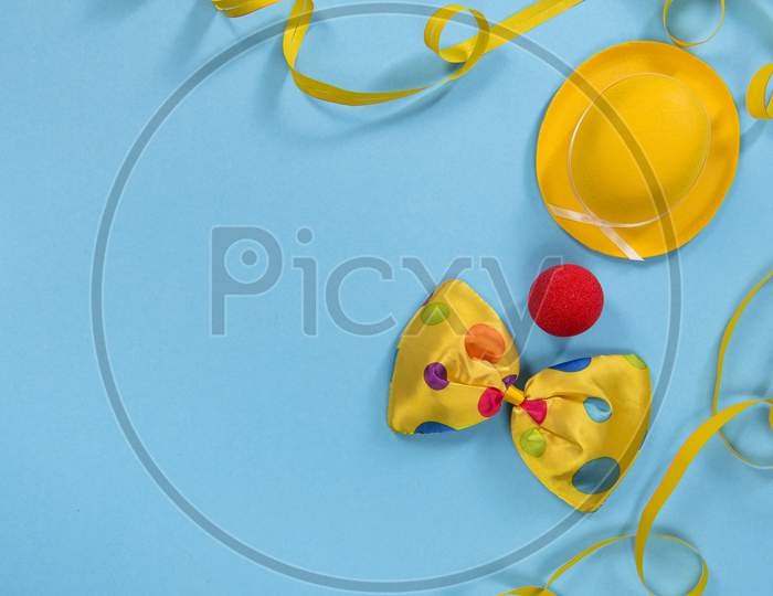 Party Flatlay With Garland, Hat, Nose And A Bow Of A Clown On A Blue Background With Space For Copy