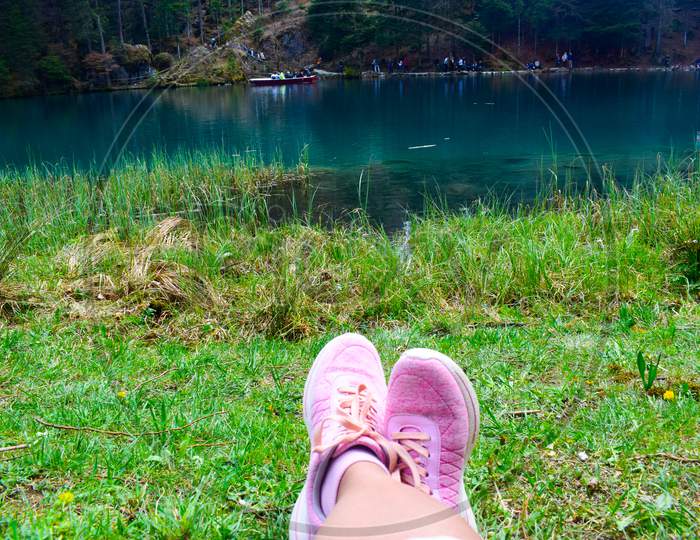 Girl relaxing near a lake with her foot stretched flaunting her new pink shoes