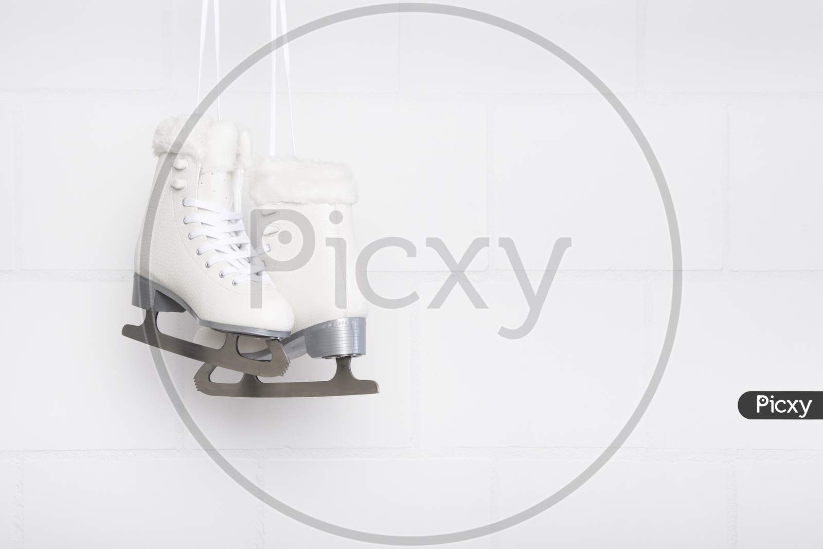 Pair Of White Figure Skates For Females Hanging At A White Concrete Background With Space For Copy