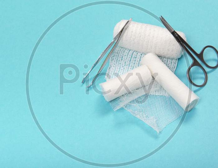 White Medical Bandages Rolls With Scissors And Tweezers In A Pharmacy Kit On A Blue Background With Space For Copy