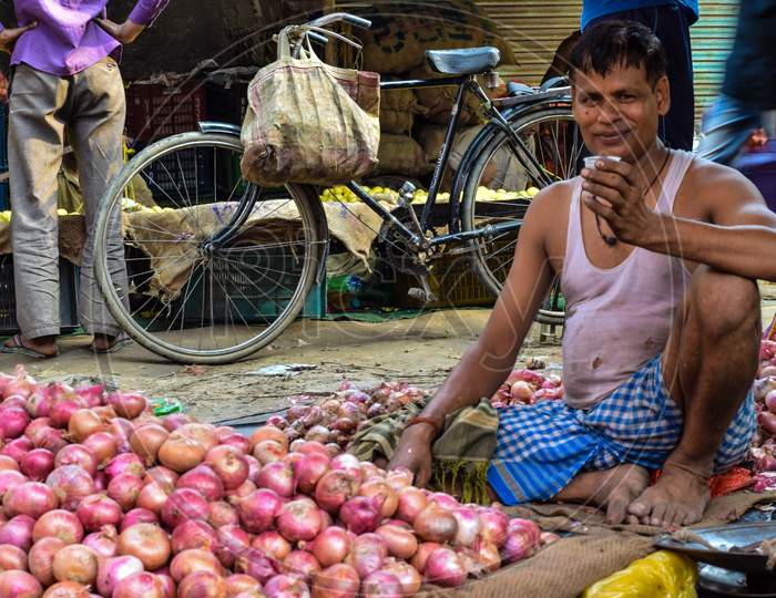 Bareilly, 2018 : Vegetable seller drinking tea and selling onions in the vegetable market. The poor vendor can be seen wearing white undershirt and blue dhoti.