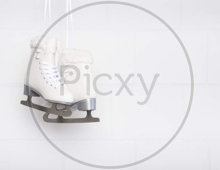 Pair Of White Figure Skates For Females Hanging At A White Concrete Background With Space For Copy