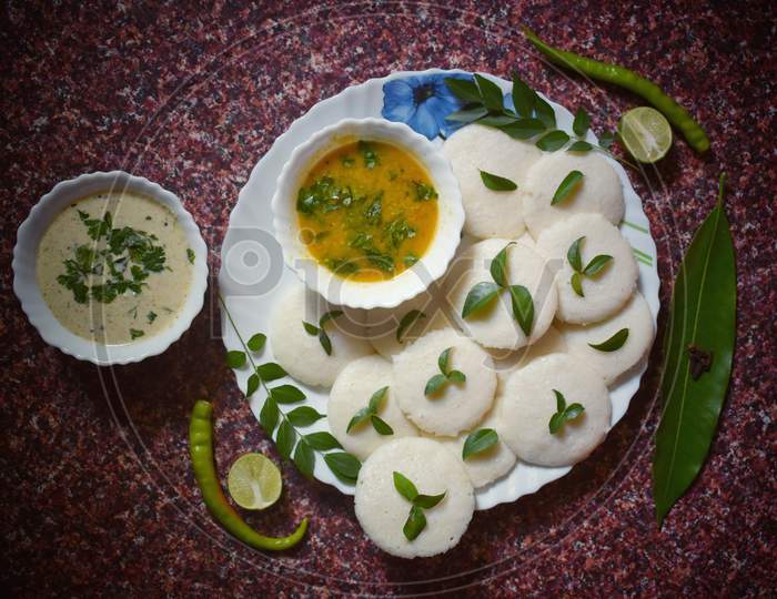 Well garnished idli, chutney and sambhar dish with the stuff of  green chillies and curry leaves and lemon