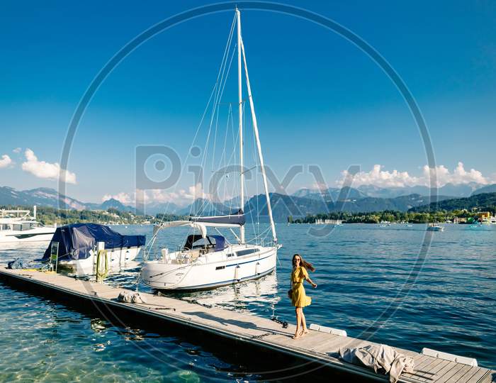 Beautiful Woman Walking On The Pier Near The Yacht And Boats With Mountains View In Europe, Switzerland
