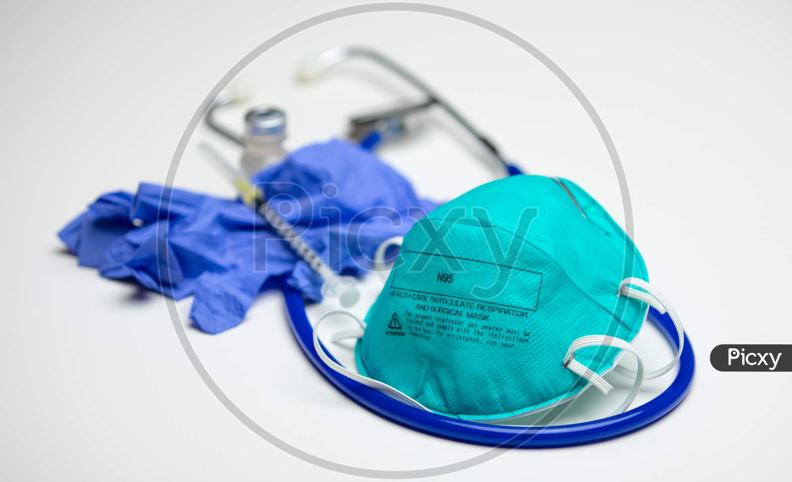 A Health Care Particulate Respirator And Surgical Mask On Top Of A Stethoscope. Gloves, Syringe And Vial In Background.