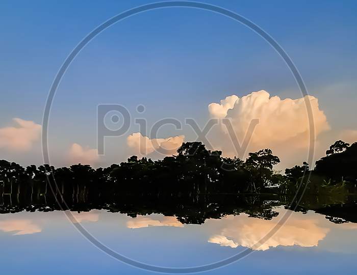 Blue Sky With White Clouds Sky And Green Trees Reflection At The Sunset Time In Indian Village Environment.