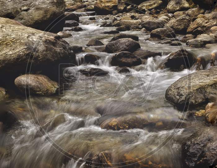 A water stream is flowing over the rocks and several trees are in the background.